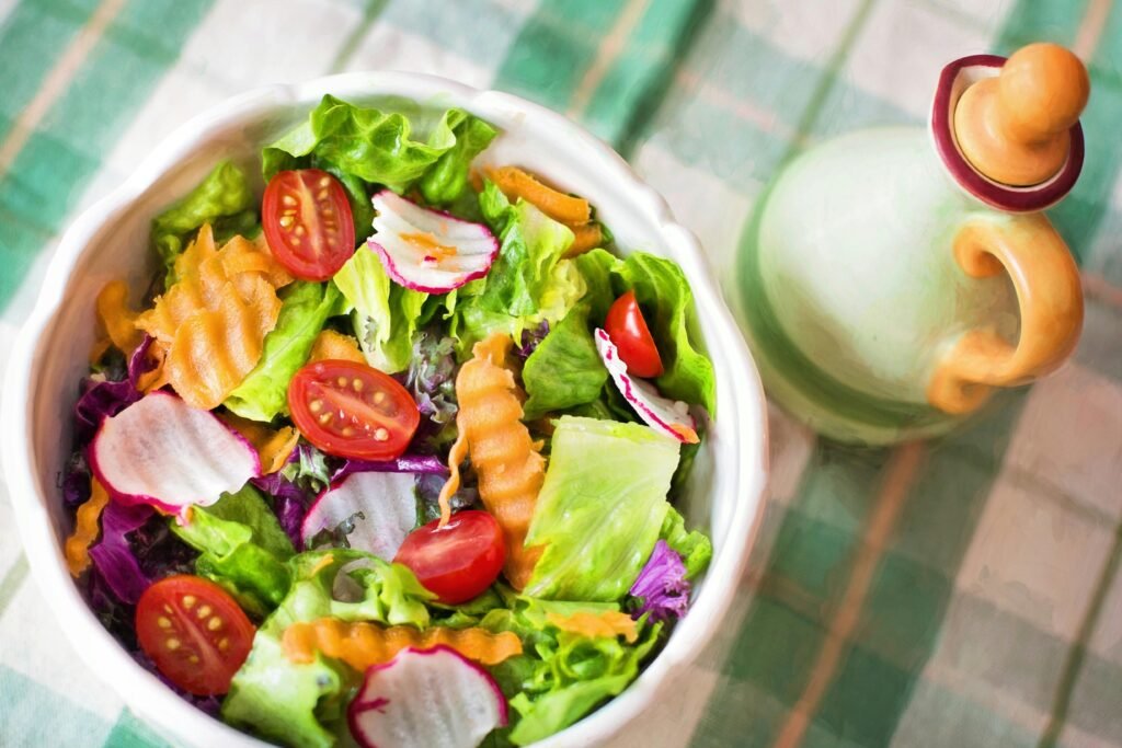 Colorful fresh salad with lettuce, tomatoes, radishes, and carrots served in a white bowl next to a decorative ceramic pot