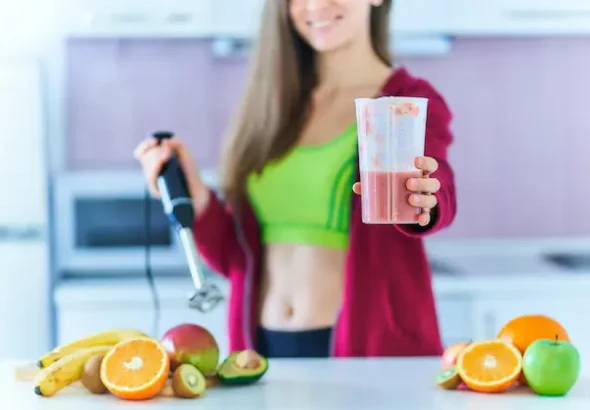 Healthy woman in sportswear preparing a fresh protein shake for weight loss, surrounded by organic fruits, in a modern kitchen.